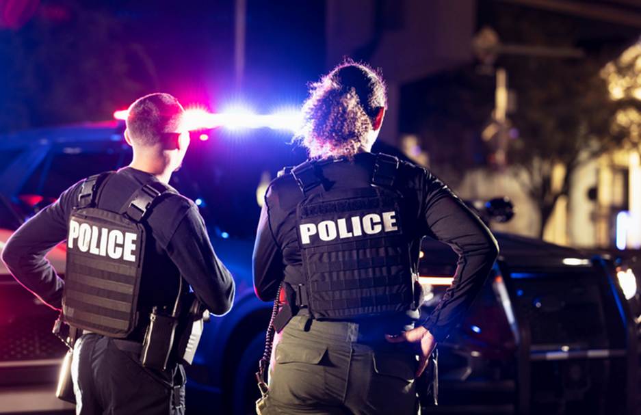 Two police officers stand by their vehicle, wearing tactical vests labeled "POLICE" in white lettering. This image accompanies content discussing civil rights attorneys.